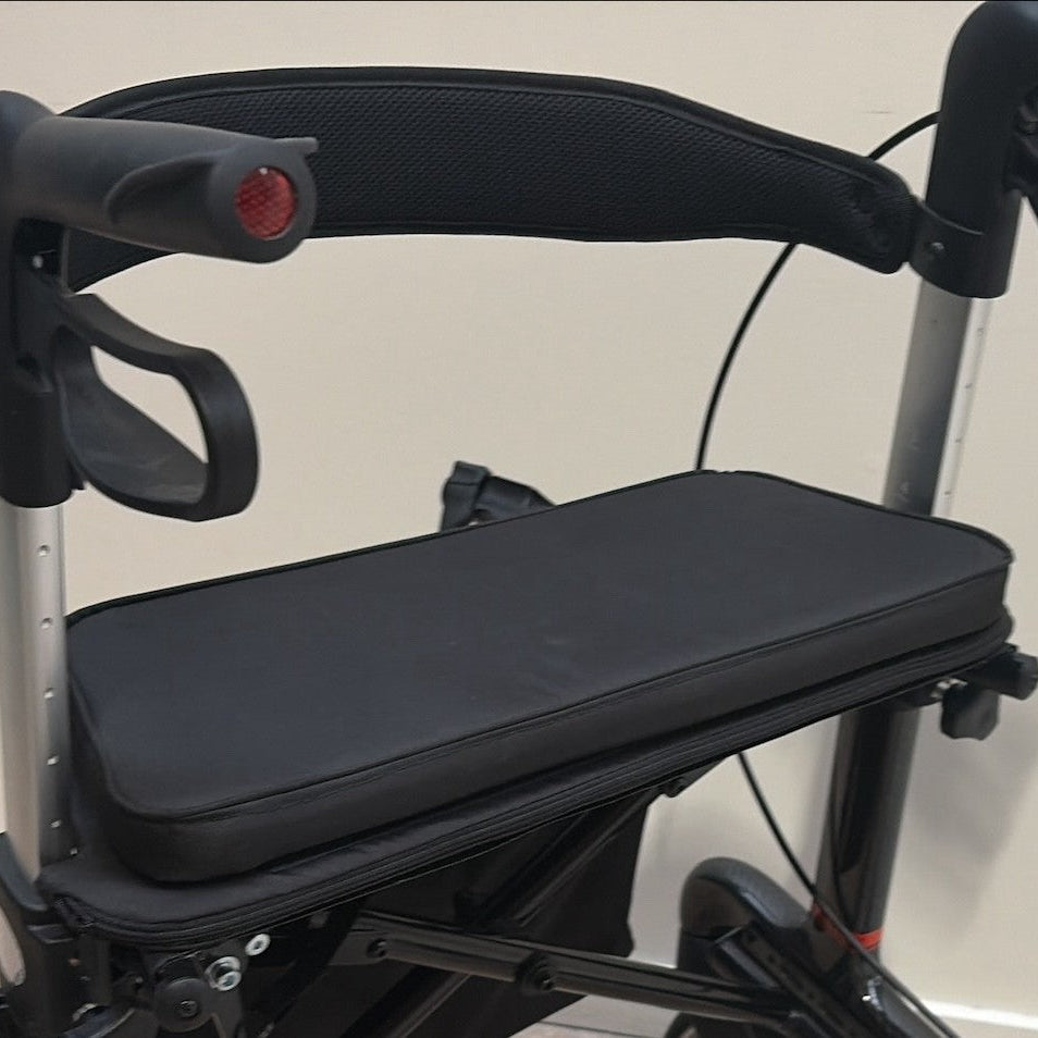 Close up of black canvas baseboard and cushion clipped over mesh seat on black Rehasense rollator; cream background.