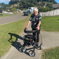Lady pushing a rollator on pavement with a residential area in the background