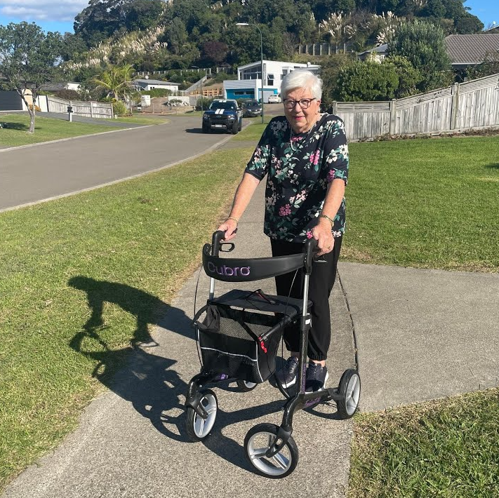 Lady pushing a rollator on pavement with a residential area in the background