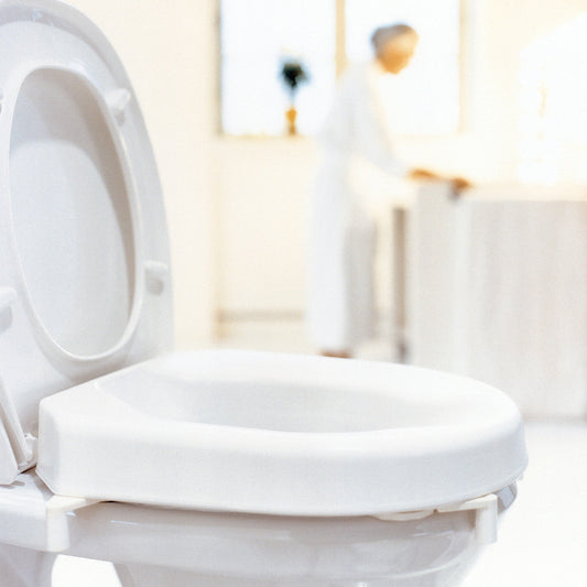 Photo of Etac Hi-loo raised toilet seat, showing the clamps and a person standing at a basin in the background