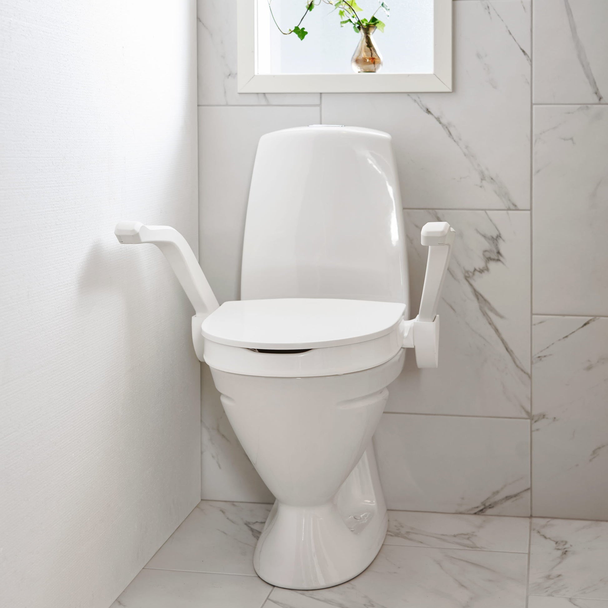 Etac My-loo raised toilet seat with armrests next to wall in bathroom