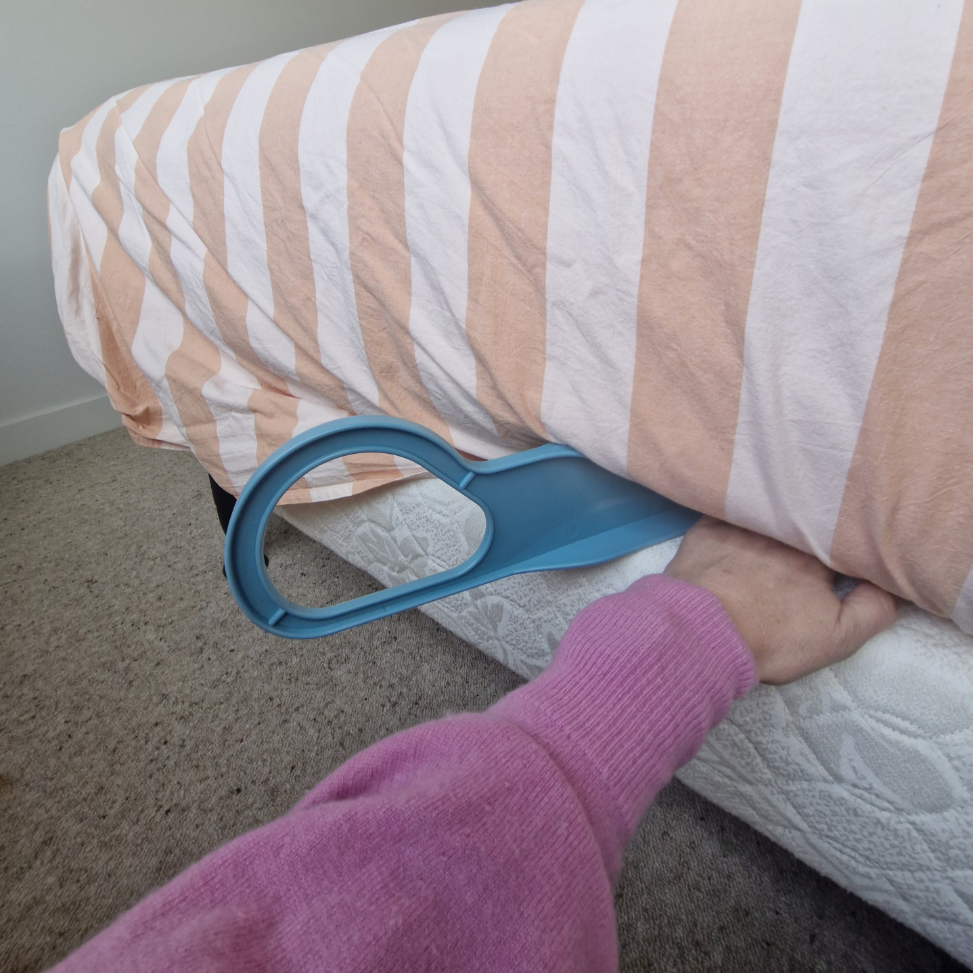Person using a blue mattress lifter to hlep push sheets between mattress and base on bed 