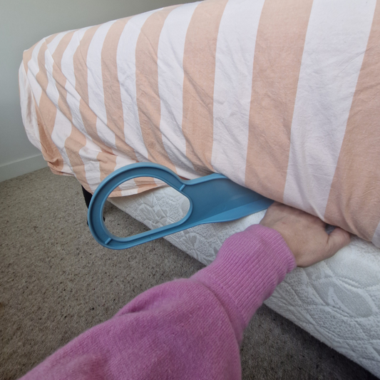 Person using a blue mattress lifter to hlep push sheets between mattress and base on bed 