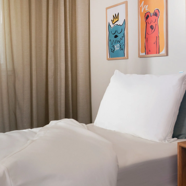 Bedroom with a bed, white pillows, and colorful wall art on a beige wall.