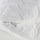 Close-up of a white quilted product with a zipper, on a light background.